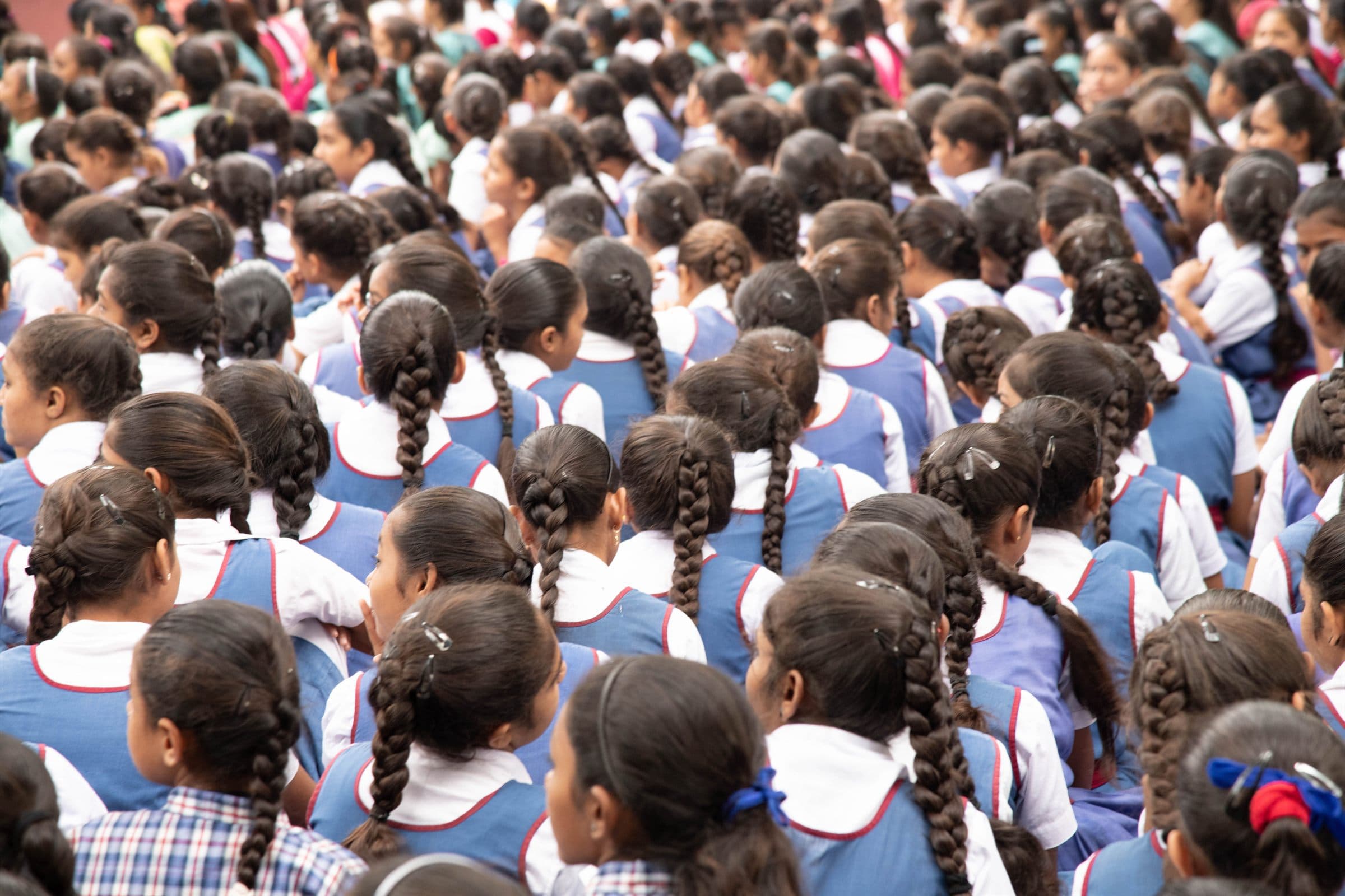 A school assembly of students in uniform seen from behind, seated in rows