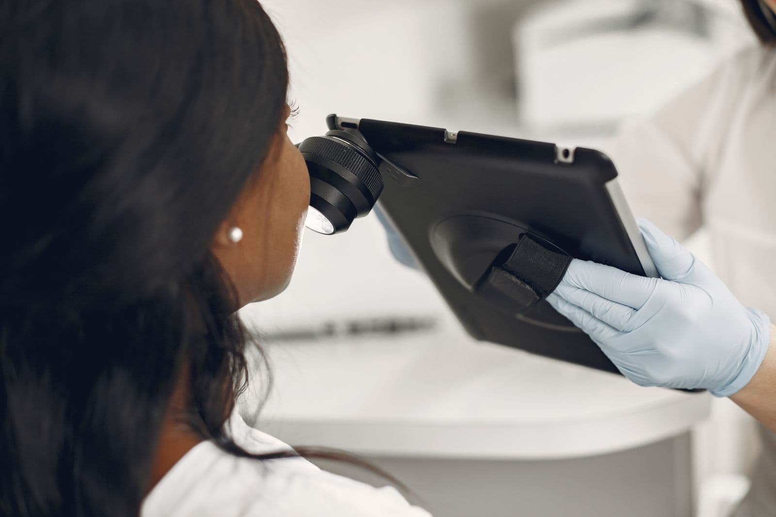 A clinician examining skin using a digital dermatoscope and tablet