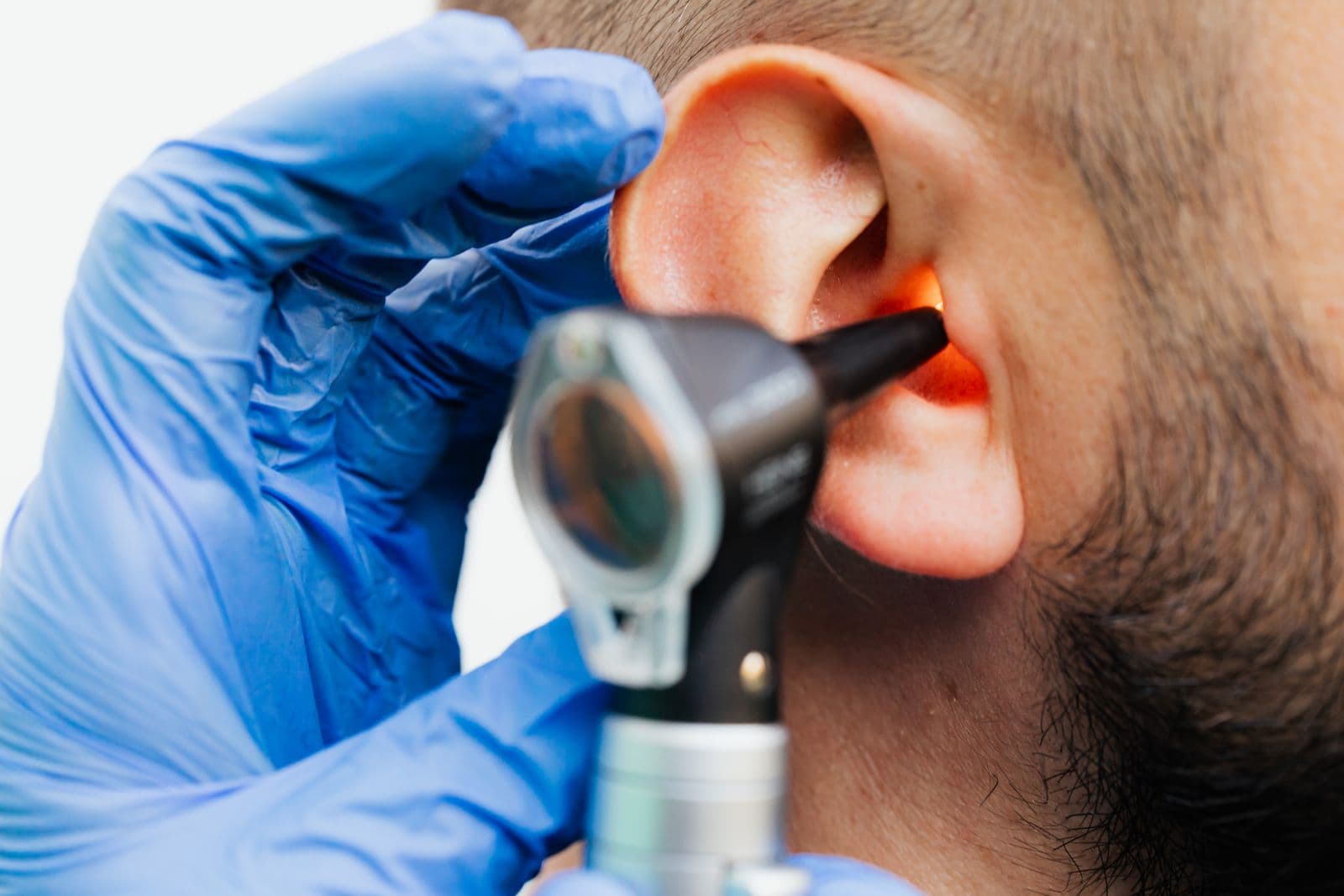 A clinician's gloved hand using an otoscope to examine a patient's ear