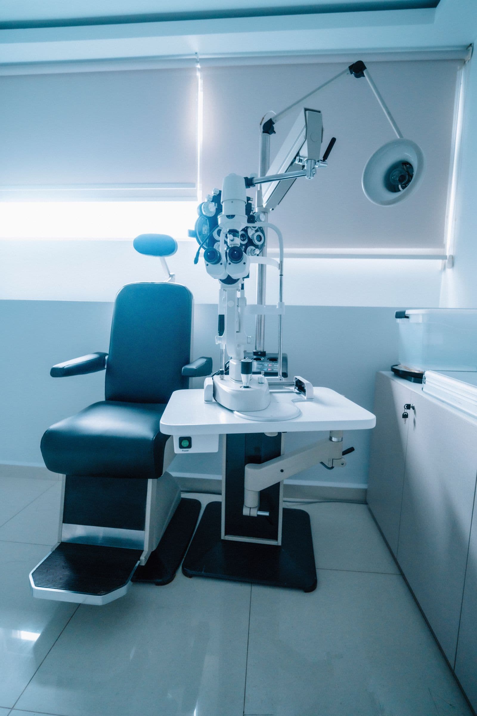 An ophthalmic examination chair beside slit lamp equipment in a clinic room
